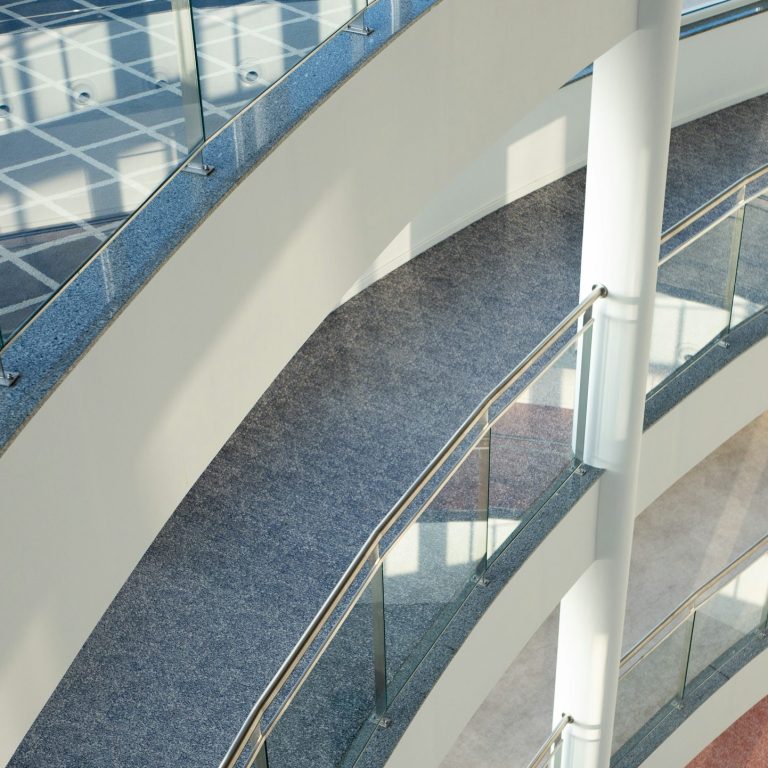 Sauberer Boden Überblick über geschwungene, moderne Treppen mit Glasgeländern und heller Beleuchtung.